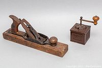 Both the antique Tre Spade FB Italian metal coffee grinder and the wooden hand plane shown together from a distance, highlighting size and condition.