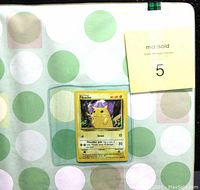 Front of the binder showing a Pikachu trading card in a clear pocket against green and white polka dot wrapping paper background.