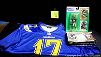 Photo showing NFL Chargers Philip Rivers blue jersey with number 17 and Starting Line-Up Deion Sanders #21 action figure in packaging with boxes of trading cards on display.