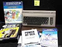 Photo showing Commodore 64 computer with visible keyboard and numeric keypad, surrounded by manuals and software booklets including 'Introduction to BASIC/Part 1,' 'Gorftek and the Microchips,' 'Power at Sea,' and 'Easy Finance V.'