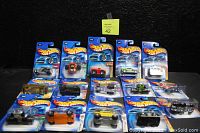 Photo showing 15 assorted Hot Wheels die-cast cars sealed on original blue card packaging on a black background, including one card with yellowed plastic bubble.