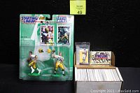 Starting Line-Up Classic Doubles Brett Favre and Bart Starr action figures with attached stands, mini helmets, and accompanying trading cards; beside an open box containing NFL Pro-Line Collection sealed pack and a large collection of assorted trading cards