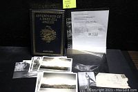 Overall view of lot items including book, photos, and notarized letter laid out on black surface.