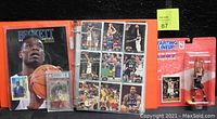 Red binder open showing multiple pages of basketball trading cards in sleeves, plus Beckett Monthly magazine and graded card visible