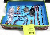 Top-down view of cultural jewelry and trinkets arranged inside Ed Hardy display box with blue interior and colorful exterior design.
