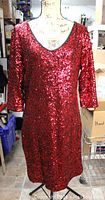 Full frontal view of the red sequin dress on a mannequin, showing 3/4 sleeves, deep V neckline, and the dress length hitting below the knees.