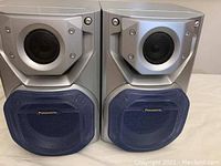 Photo showing front view of two Panasonic speakers with blue fabric bass covers.