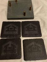 Four engraved Canadian slate coasters arranged side by side showing engraved logos and natural rough edges.