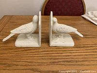 Pair of white painted cast-iron bird bookends facing each other on a table, showing overall shape and size.