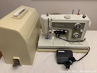 Full front and side view of Kenmore sewing machine model 19371 with attached foot pedal and separate beige hard plastic carrying case.