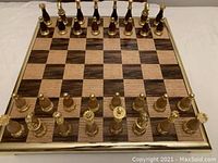 Top-down view of the full chessboard showing gold-colored metal frame and alternating wooden squares with all gold-colored metal pieces arranged at start position
