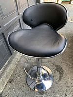 View of the full chair showing black vinyl seat, curved back, round chrome base and chrome footrest with noticeable wear and minor pitting on metal parts.