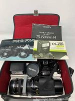 Photo of Yashica camera bodies, lenses, flash, and instruction manuals arranged inside a carrying case with red interior.