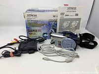 Photo showing Hitachi DZ-MV550A DVD Handy Cam with manual, original box, and various cords and accessories laid out on white surface.