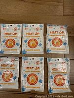 Front view of six individual Heat Up hand warmer packages, each labeled with usage time of 12+ hours and type 'Hand Warmers'.