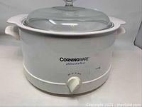 Full view of white CorningWare Electrics 6 quart electric cooking pot with clear glass lid and side handles.