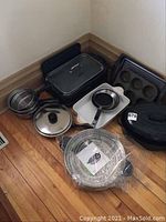 Photo showing the collection of kitchenware and cookware items including smokeless grill, roasting pan, pots, baking trays, steaming pan, and frying pan grouped on floor.