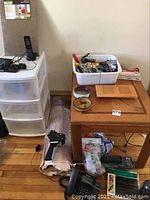 Wooden side table holding various items including tools and vent covers, with drawers and office supplies beside it.