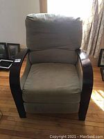 Front view of a greenish-beige fabric recliner chair with dark wood arm rests showing the seat, back, and headrest cushions.