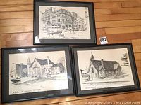 Three framed black and white etchings showing architectural scenes: city street and two churches.