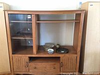 Full frontal view of wood entertainment TV cabinet with open center shelf, glass display cabinet on left, and lower drawer with doors.