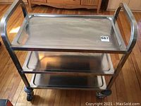 Front view of the metal kitchen cart showing all three stainless steel shelves and handles.