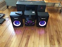 Front view of Headrush stereo system with central unit and two speakers lit with LED lights on wooden floor