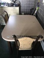 Top view of rectangular kitchen table with leaf extension, showing light beige speckled surface and thick brown metal legs, with one matching chair.