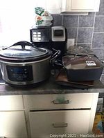 Wide angle view of kitchen countertop showing all the kitchen appliances and cookware in the lot, including crock pot, coffee maker, pan with lid, deep fryer and grill