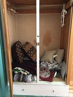 Photo of the linen items inside a closet including blankets and pillows stacked inside.