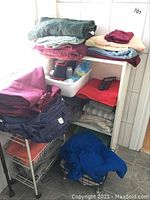 Full view of metal shelving unit with towels, blankets, white bin with liquids, red cane, and metal cart on bottom left