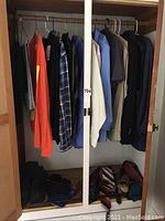 Full view of closet containing hanging men's shirts, jackets, and vests in size XL along with folded clothing and accessories below