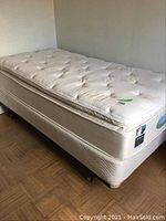 Full view of the assembled twin bed with mattress and boxspring, showing the mattress tag and pillow top quilted design.