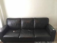 Front view of the black leather sofa showing three seats, visible tear on one cushion.