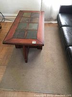 Coffee table positioned on the beige area rug, showing scratches, nicks, and wear on the table edges, plus visible wear on the rug.