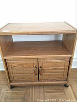 Front view of wood TV stand showing top flat surface, open middle shelf, and lower double-door cabinet on castors with visible wear.