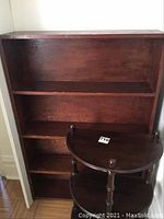 Full view of rectangular wooden bookshelf with three shelves, showing wood grain and condition with wear at edges.