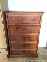 Front view of wooden highboy dresser showing five drawers, with carved design on the top drawer and a mix of round knobs and recessed pulls. Visible wear on drawer fronts and edges.