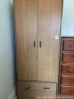 Front view of wooden wardrobe with two doors and a lower drawer showing drawer handles and wood grain.