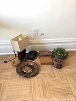 Wide view of all items in the lot displayed on wooden parquet floor against white wall including lamp, wooden boxes, alarm clock, coasters, nutcracker, and planter pot with succulents.
