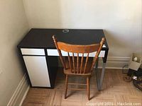 Front view of black desk with side drawer, top drawer, cable hole; wooden chair placed in front.