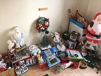 Photo showing an assortment of Christmas decorations including figurines, wreath, inflatable Santa, string lights, mugs, and ornaments.