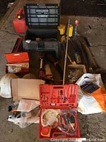 Wide angle photo showing overall lot with items including tool boxes, hard hats, gas cans, painting supplies, and various hand tools arranged on a concrete floor.