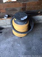 Yellow Genie SV300Q shop vacuum in a corner, with hose wrapped around base.