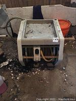 Photo showing full front view of large garden hose reel unit on the ground, surrounded by dirt and debris, with attached hose visible.