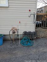 Photo showing overall lot contents lined up against house wall: metal garden borders with signs, green garden hose, black metal garden border sections, shepherd's hook, and measuring stick.