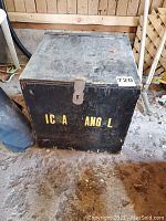 Closed black metal storage box with yellow letters and hinged lid in a wood interior setting.