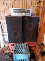 Stereo receiver resting on top of two speakers with one speaker cover showing damage.