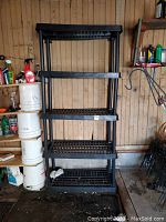 Full view of black plastic shelving unit against a wall, showing five vented shelves made of black plastic with vertical support columns.