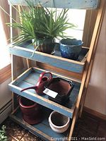 Live aloe plant in a brown decorative ceramic pot with attached saucer, blue ceramic pot beside it, displayed on a wooden blue-painted shelf
